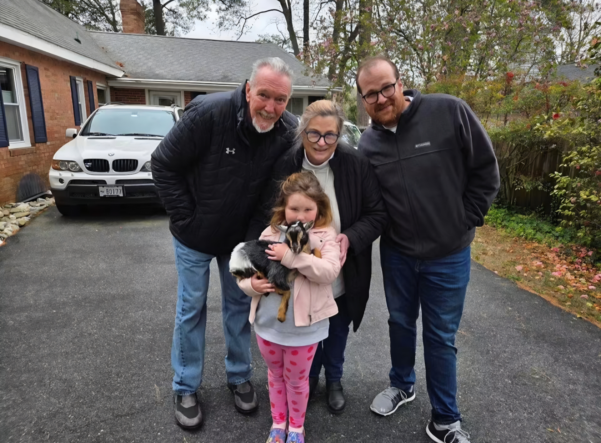 Young girl holding a goat with three adults standing around her outdoors